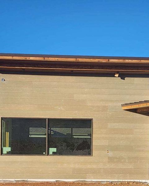 Beige exterior wall with dark-framed window, wooden trim, and clear blue sky.