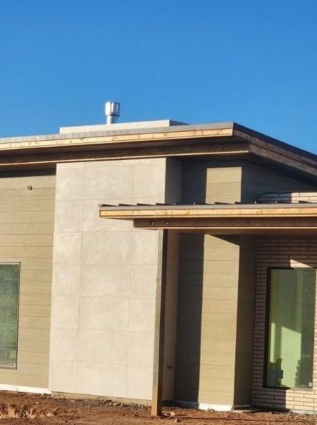 Modern beige home exterior with a rectangular chimney and a flat roof against a clear blue sky.