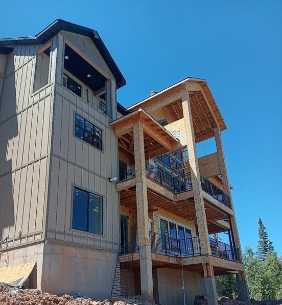 Multi-story house under construction with exposed beams, balconies, and blue sky.