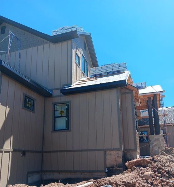 Construction of a beige house with dark trim under a bright blue sky. Scaffolding visible.