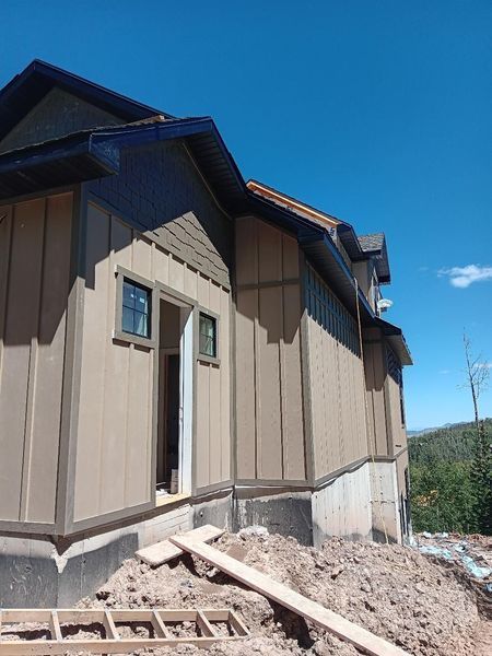 Tan and brown house exterior under construction with dark blue trim against a blue sky.