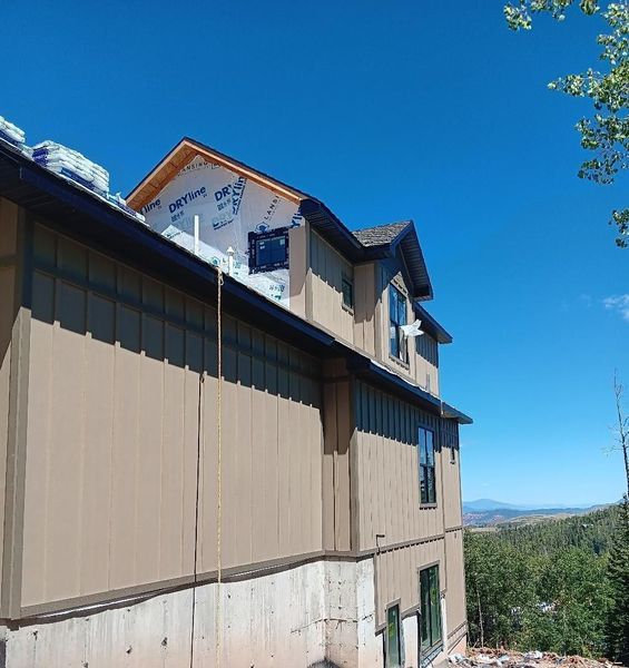 Beige house under construction with blue sky, surrounded by trees and a mountain in the distance.
