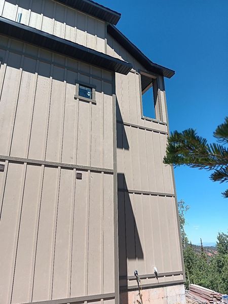 Side of a house with brown siding and trim, against a clear blue sky.