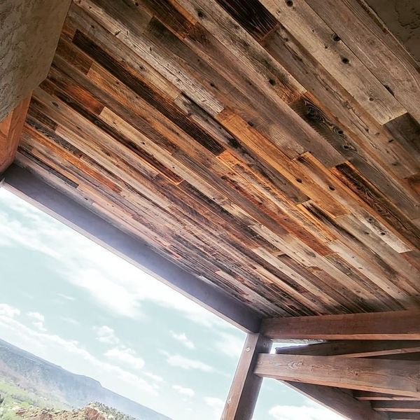 Wooden planks on a porch ceiling with a view of the sky and mountains.