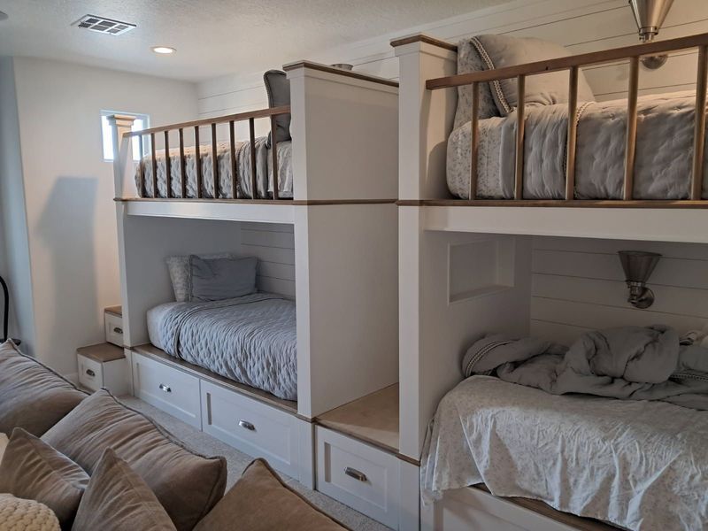 White bunk beds with drawers and wooden railings. Gray bedding and pillows.