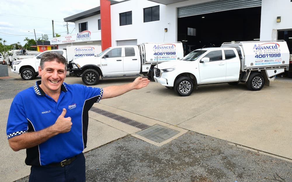 Man in Blue Shirt Points to White Service Trucks — Advanced Auto Electrics & Mechanical in Innisfail, QLD