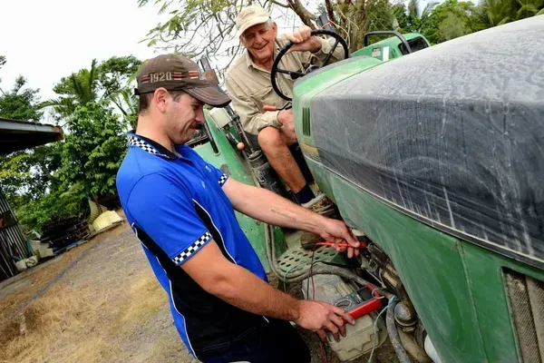 Man in Blue Shirt Works on Tractor Engine While Another Man — Advanced Auto Electrics & Mechanical in Innisfail, QLD