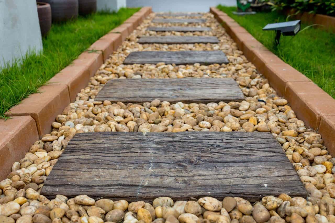 A Wooden Walkway Lined With Rocks And Bricks In A Garden — Envy Landscape Supplies In Urangan, QLD