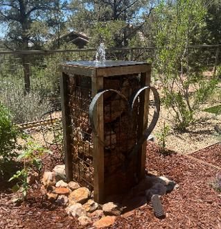 Outdoor water fountain with wooden frame, stone and metal accents, and a small water spout.