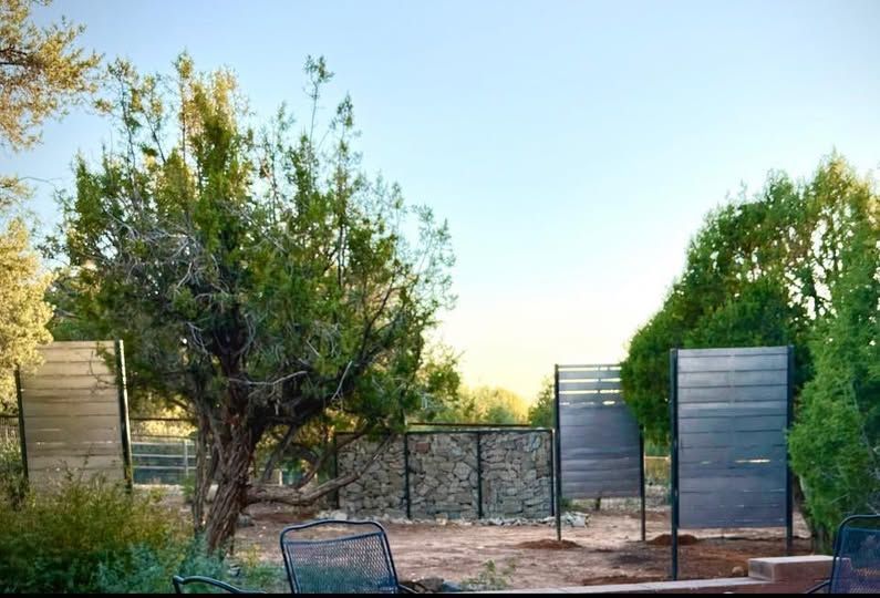 Outdoor area with wood and stone fences, trees, and blue sky.