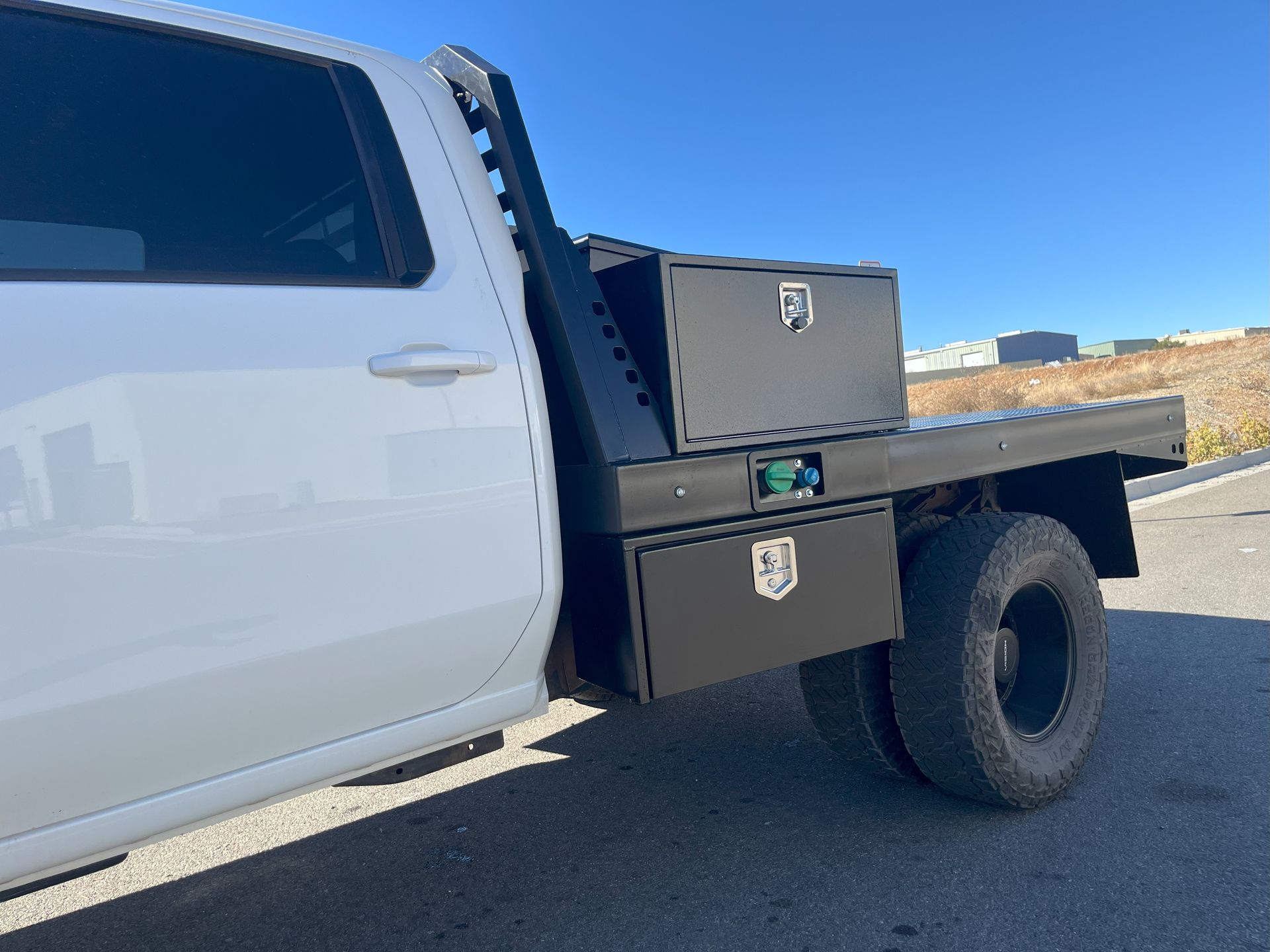 White pickup truck with a black flatbed and storage boxes parked outside on a sunny day.