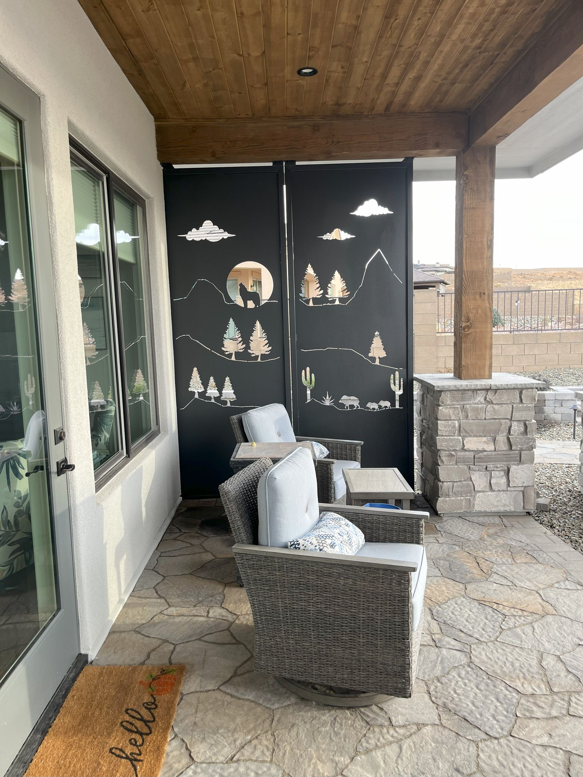 Patio with black laser-cut privacy screen featuring a desert scene, seating area, and stone flooring.