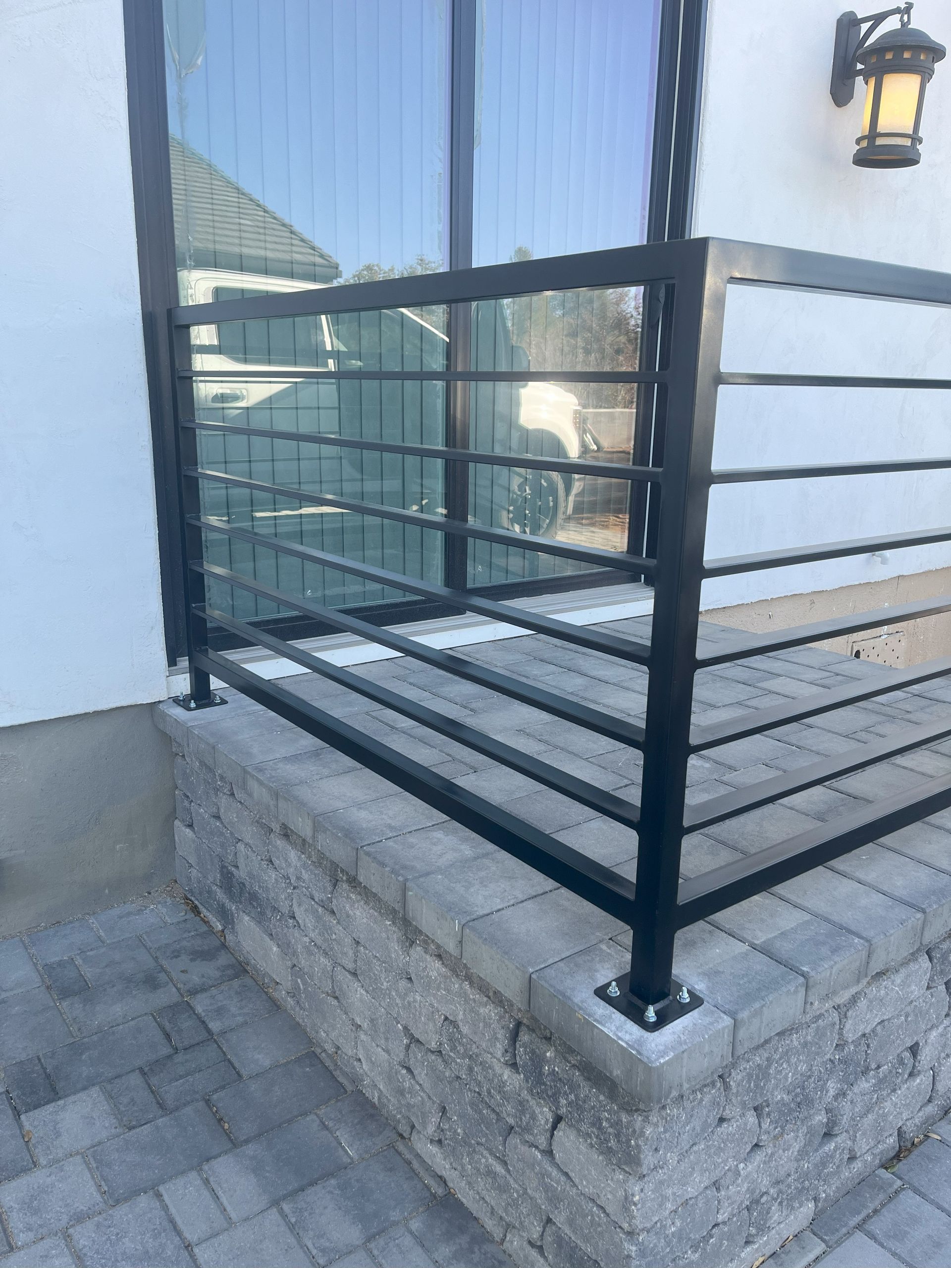 Black metal railing on a brick step next to a window and white wall.