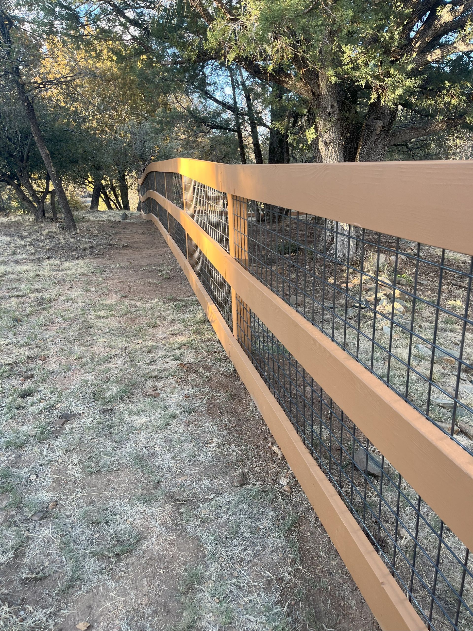 A brown wooden fence with wire mesh in a wooded area.