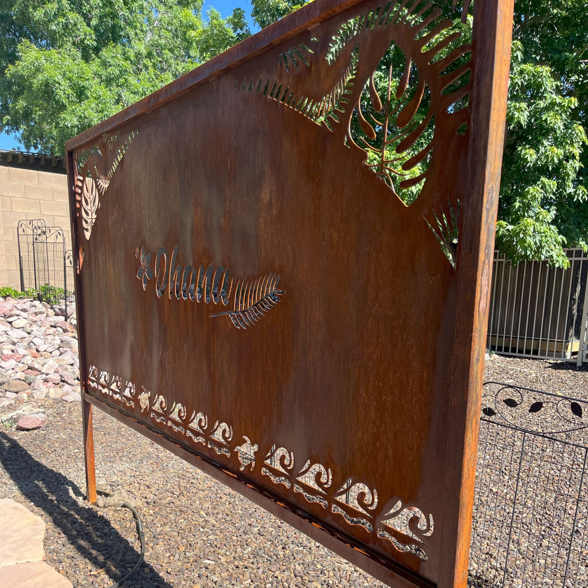 Rusty metal garden screen with leaf and wave cutouts, placed outdoors.