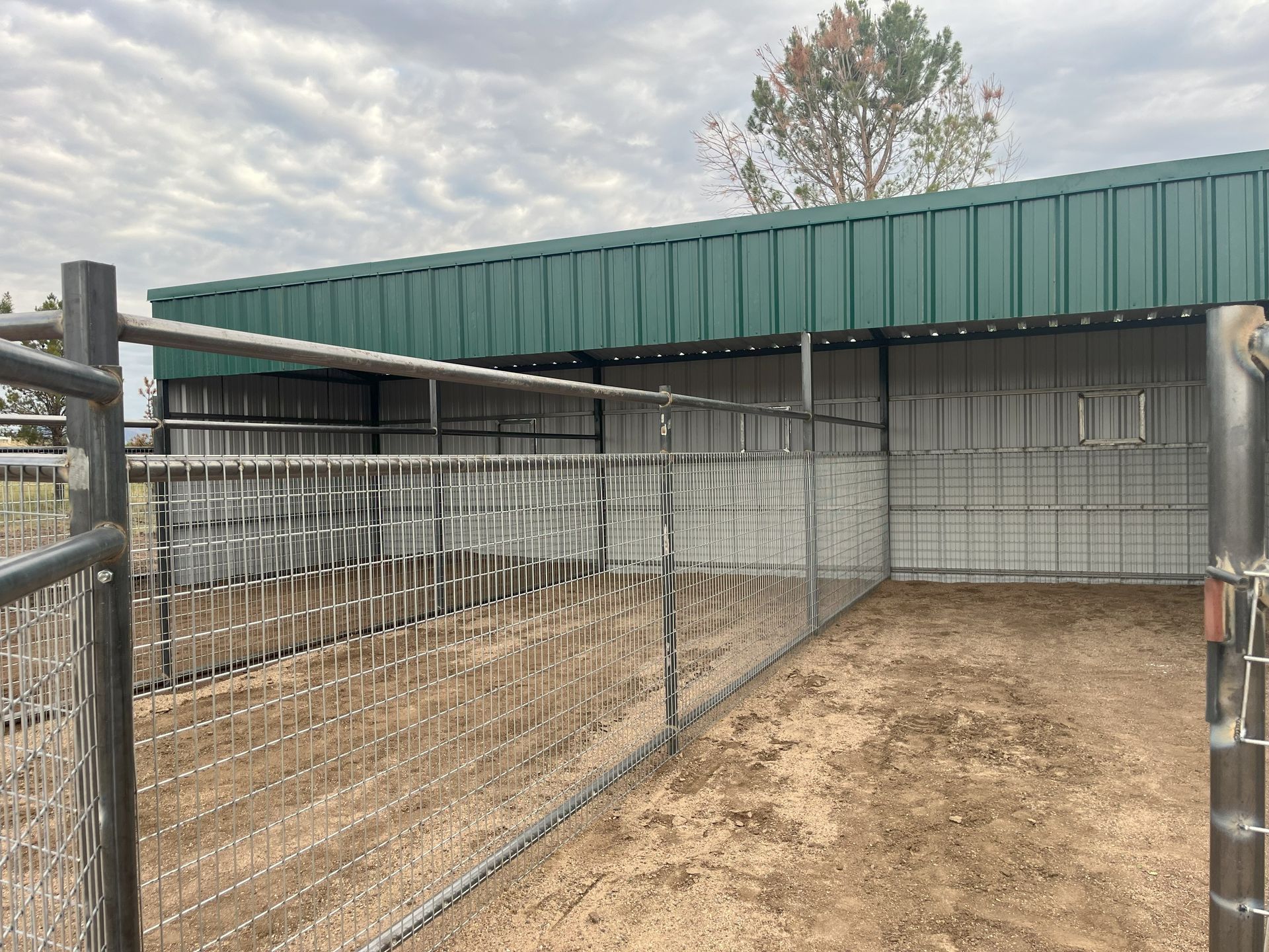 A metal animal pen with a green roof, constructed with metal fencing and an open entrance.