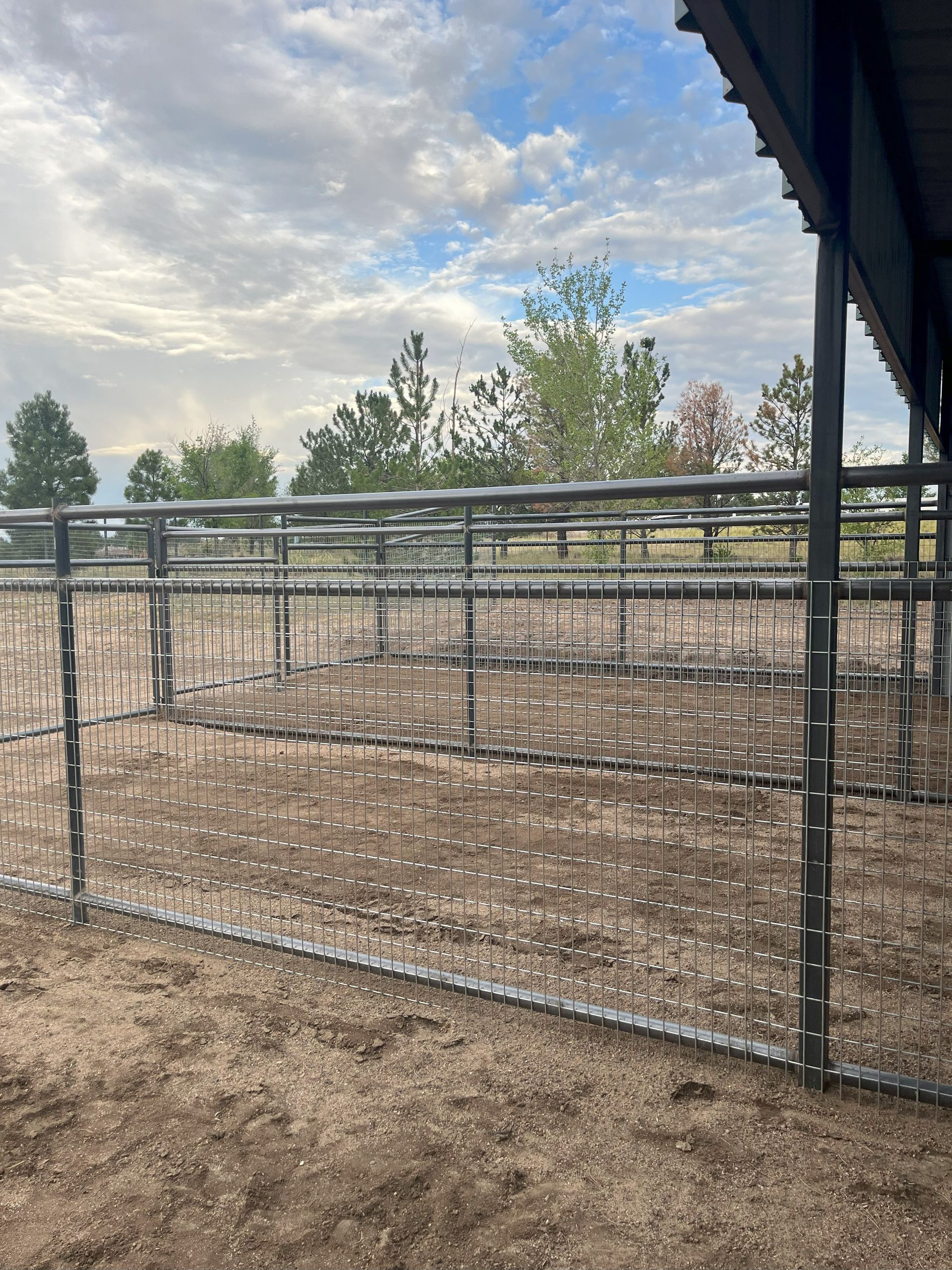 Metal horse stalls in an outdoor stable with cloudy sky.
