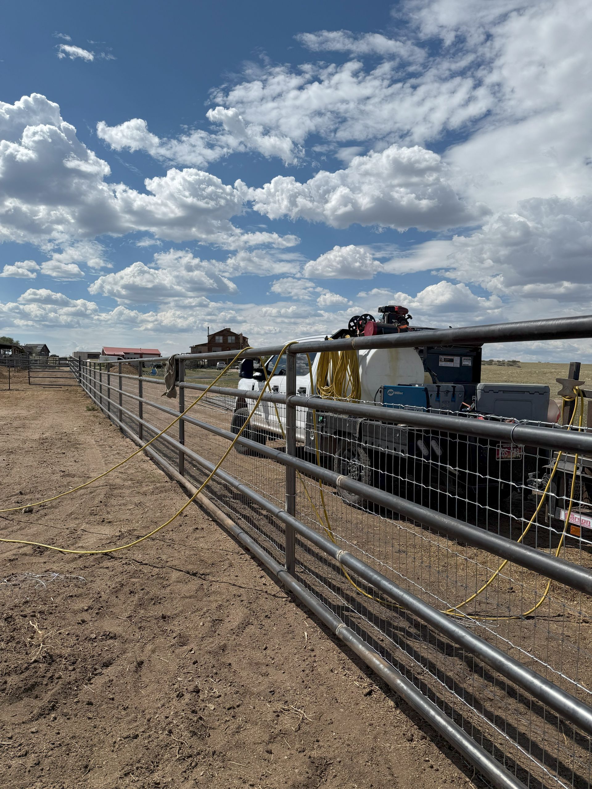 Metal fence along dirt path, vehicle parked behind it, under a cloudy blue sky.