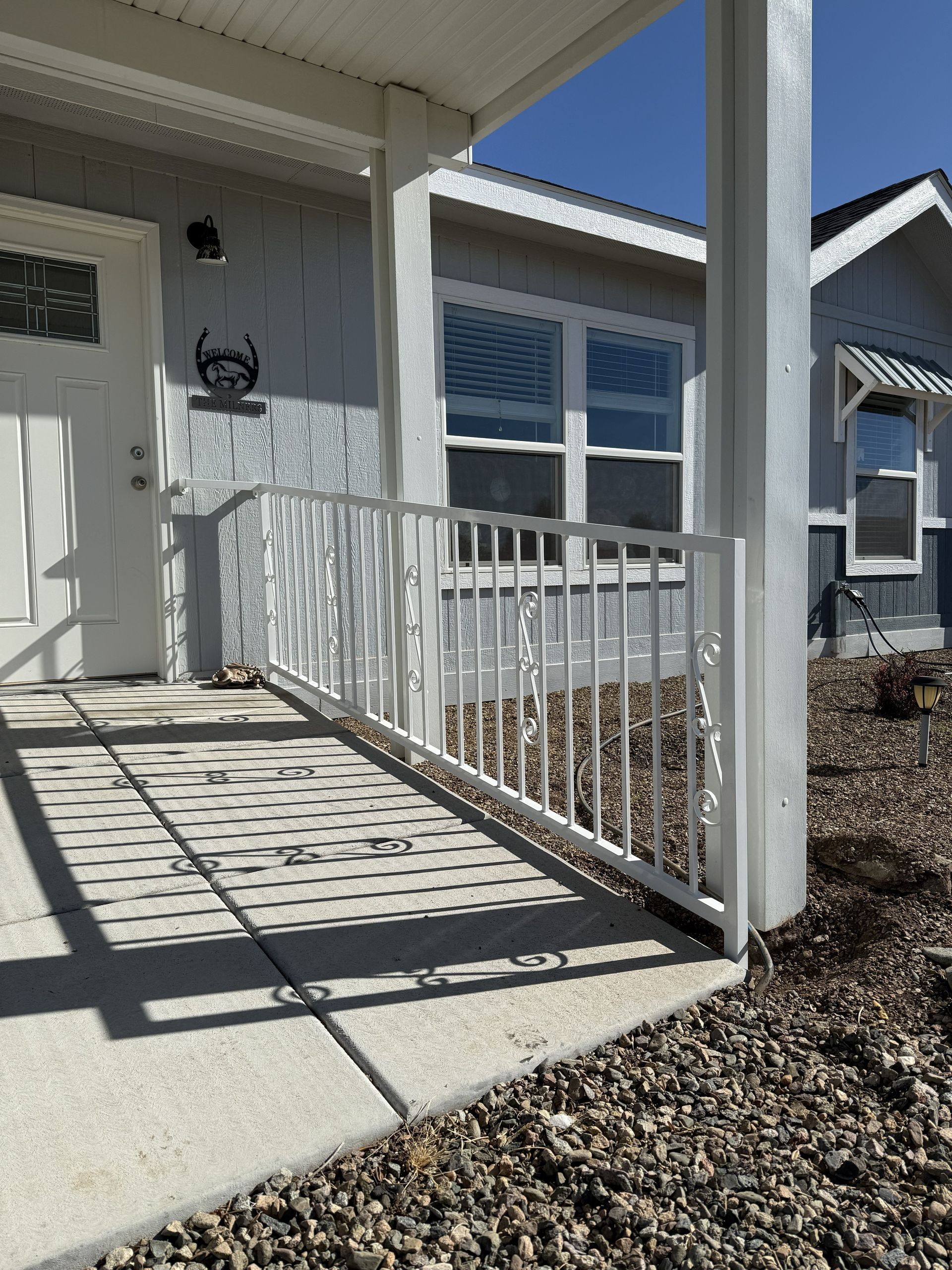 White metal railing on a concrete porch ramp leading to a gray house front door.