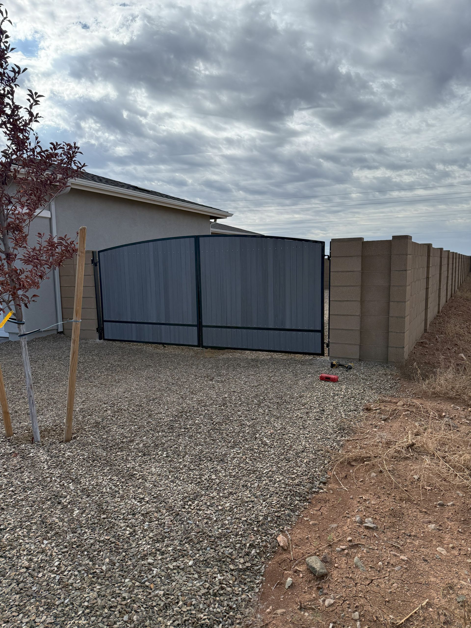 Backyard entrance with a gray privacy screen gate, gravel ground, and a block wall.