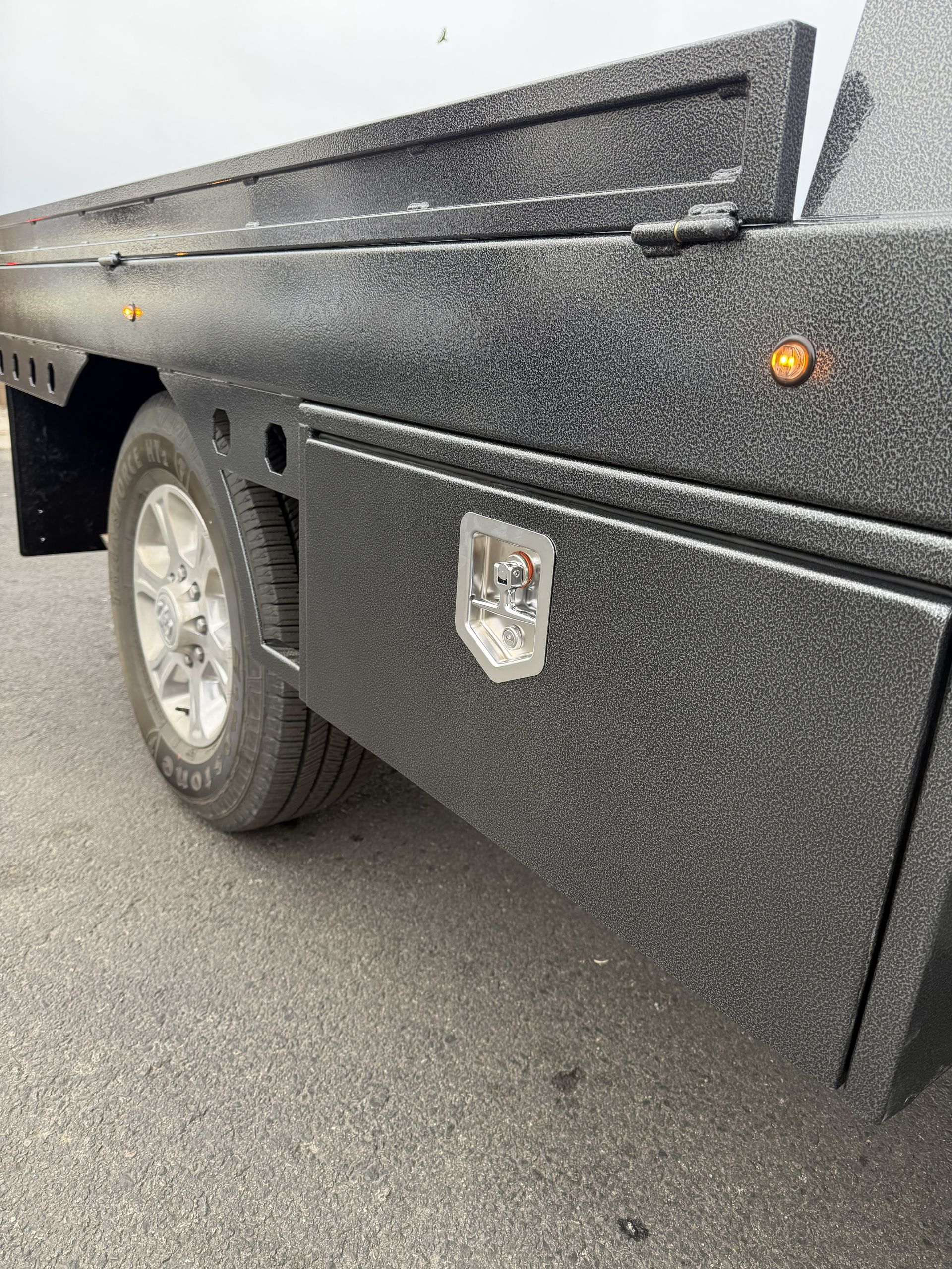 Close-up of a truck's textured black side panel featuring an integrated storage compartment with a chrome handle.