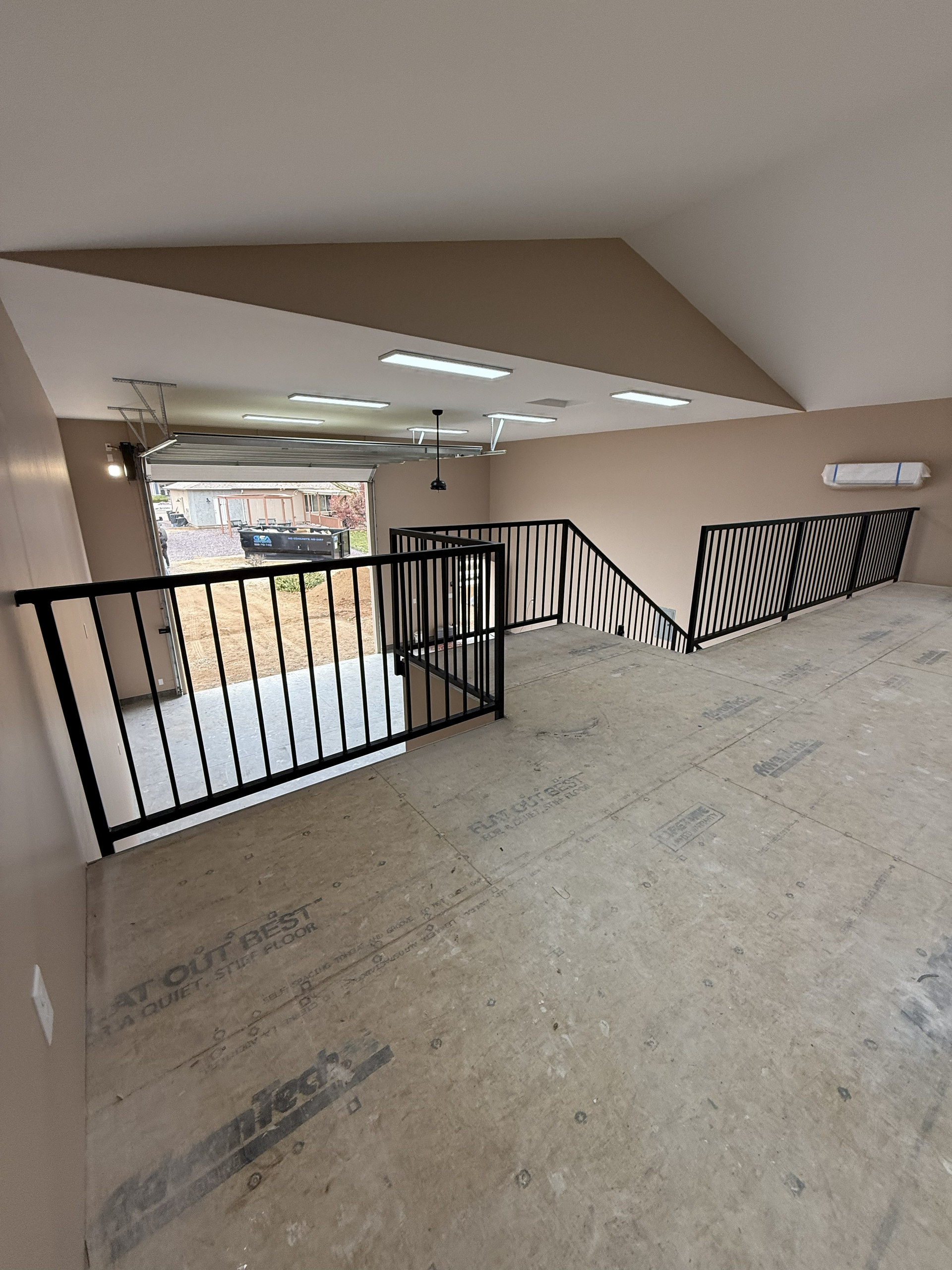 Interior view of a loft with a black railing, patterned wall, and exposed concrete floor.