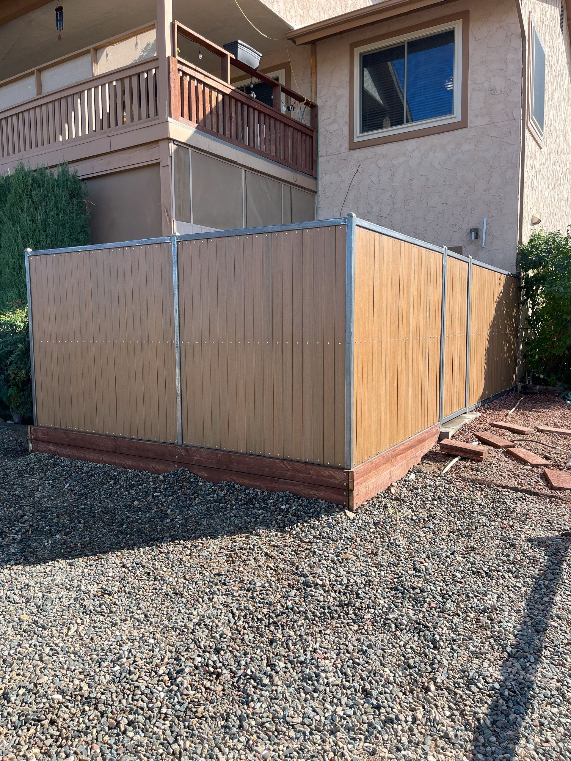 Tan privacy fence built on a gravel ground next to a building.