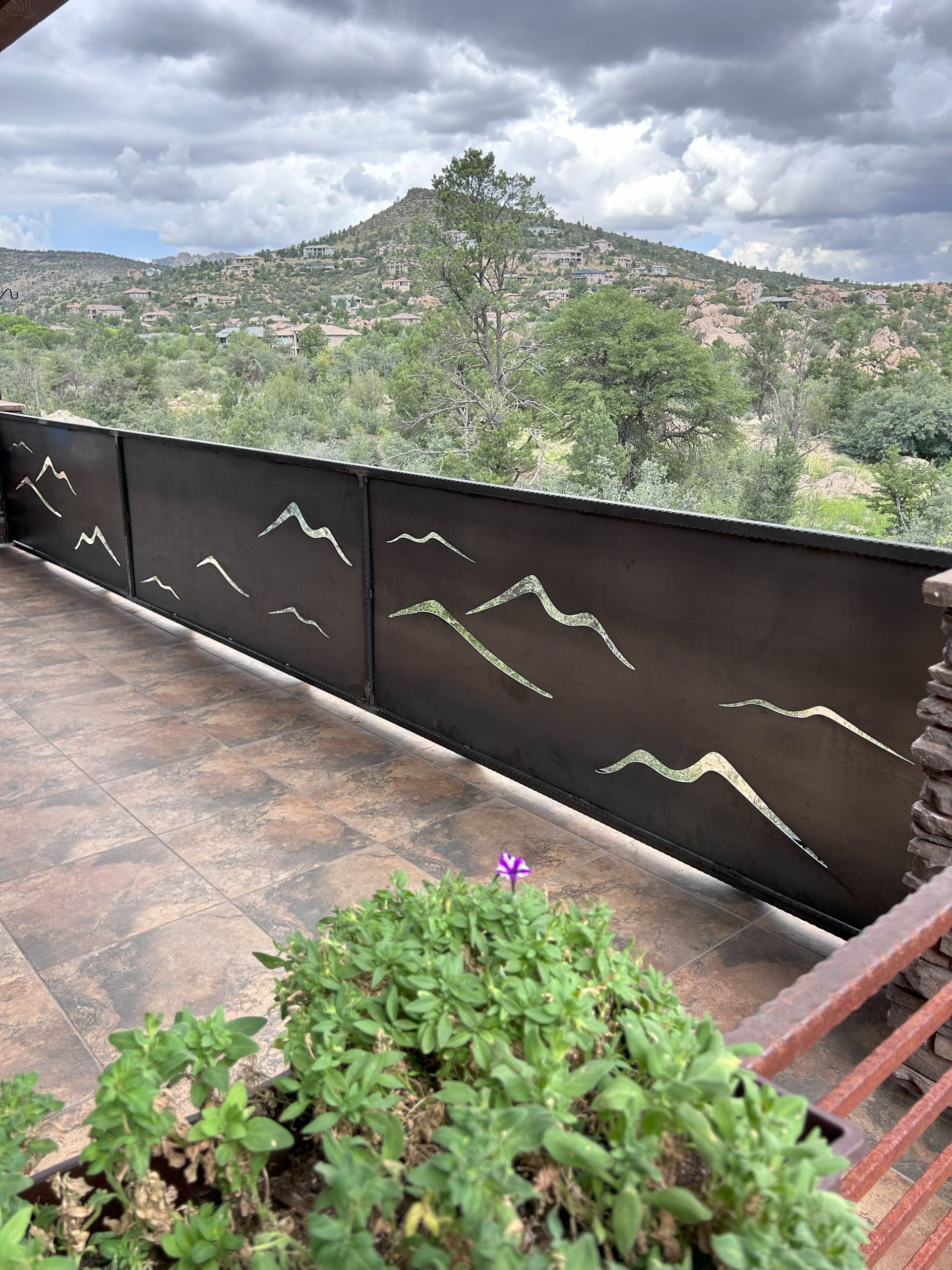 Brown metal fence with mountain cutouts, overlooking a mountain range and greenery.