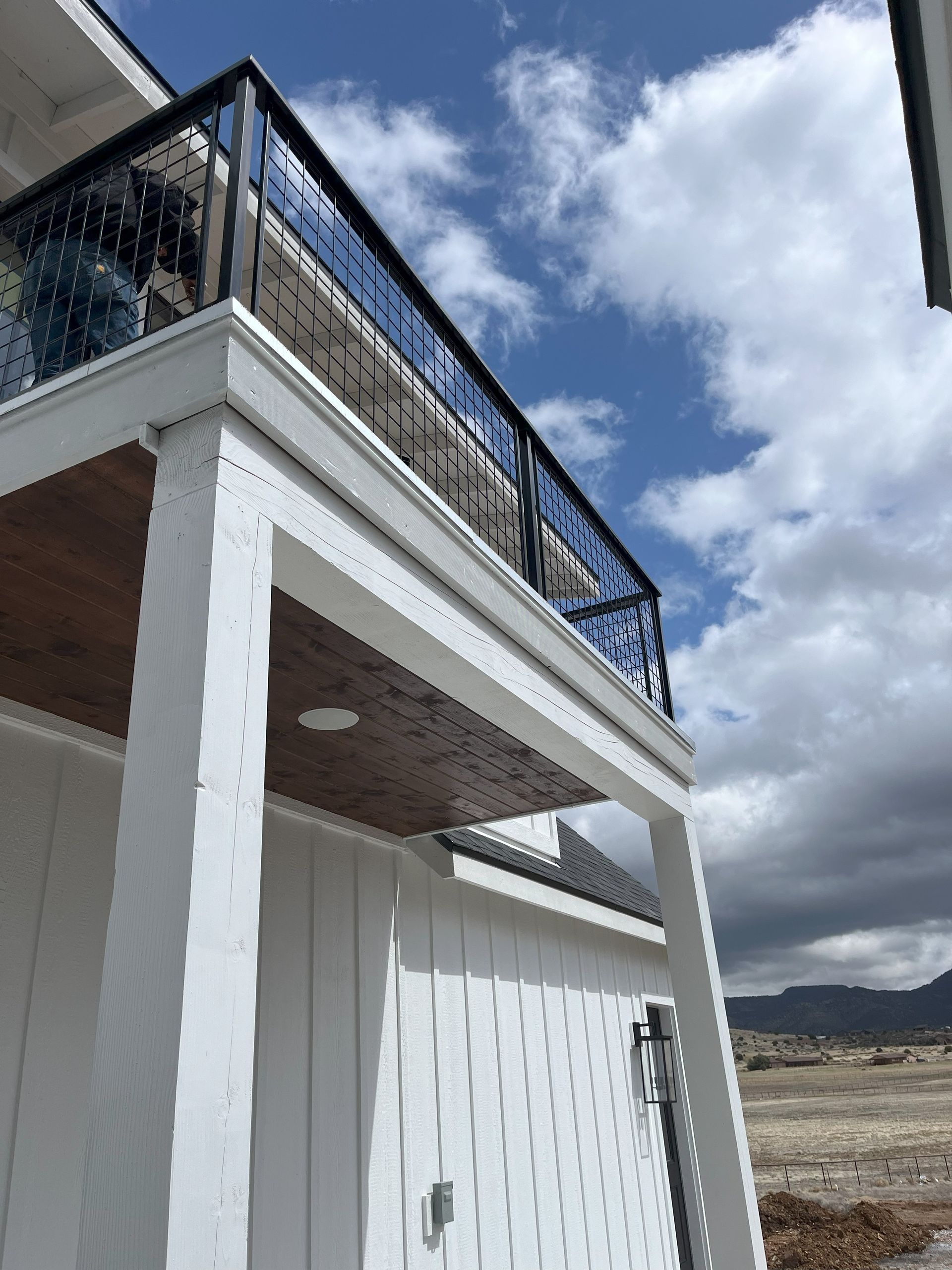 White building with a black balcony railing against a blue sky with clouds.