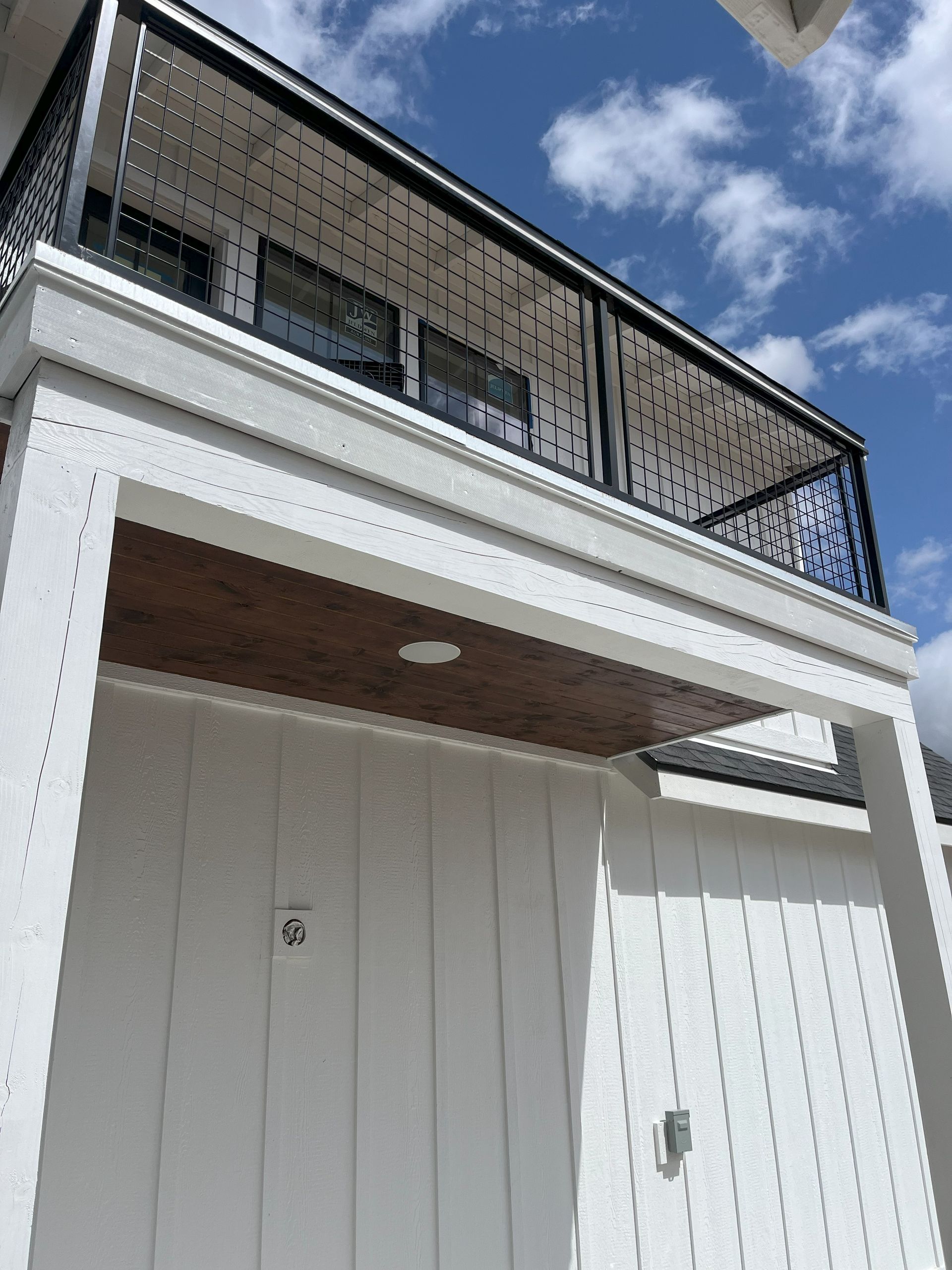 White building with black railing balcony and wooden ceiling under blue sky.