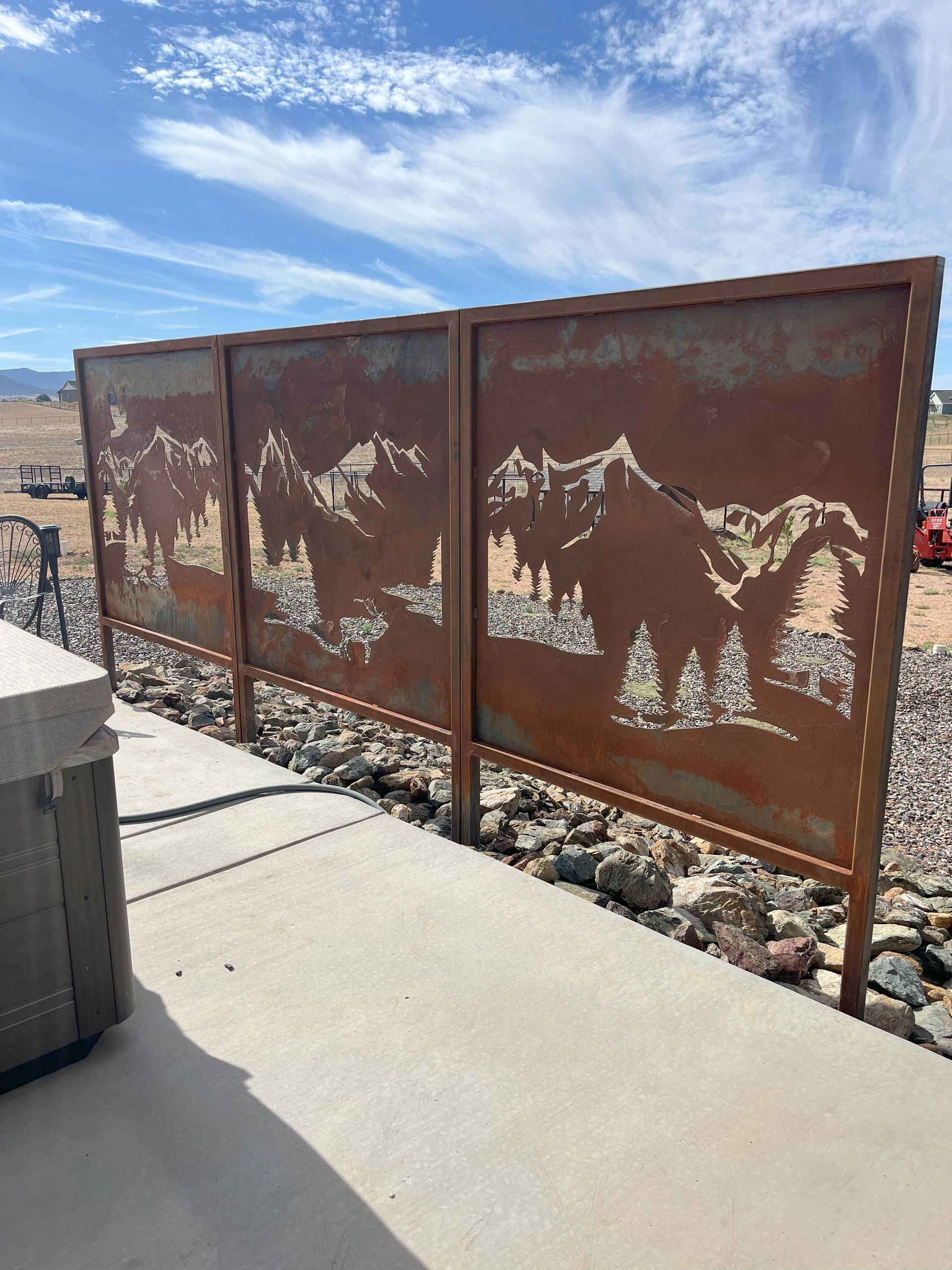 Rust-colored metal privacy screen with mountain and tree cutouts on a concrete patio.