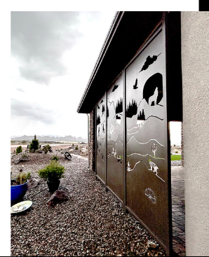 Metal screen with cut-out landscape designs, next to a building with a gravel bed and desert plants.