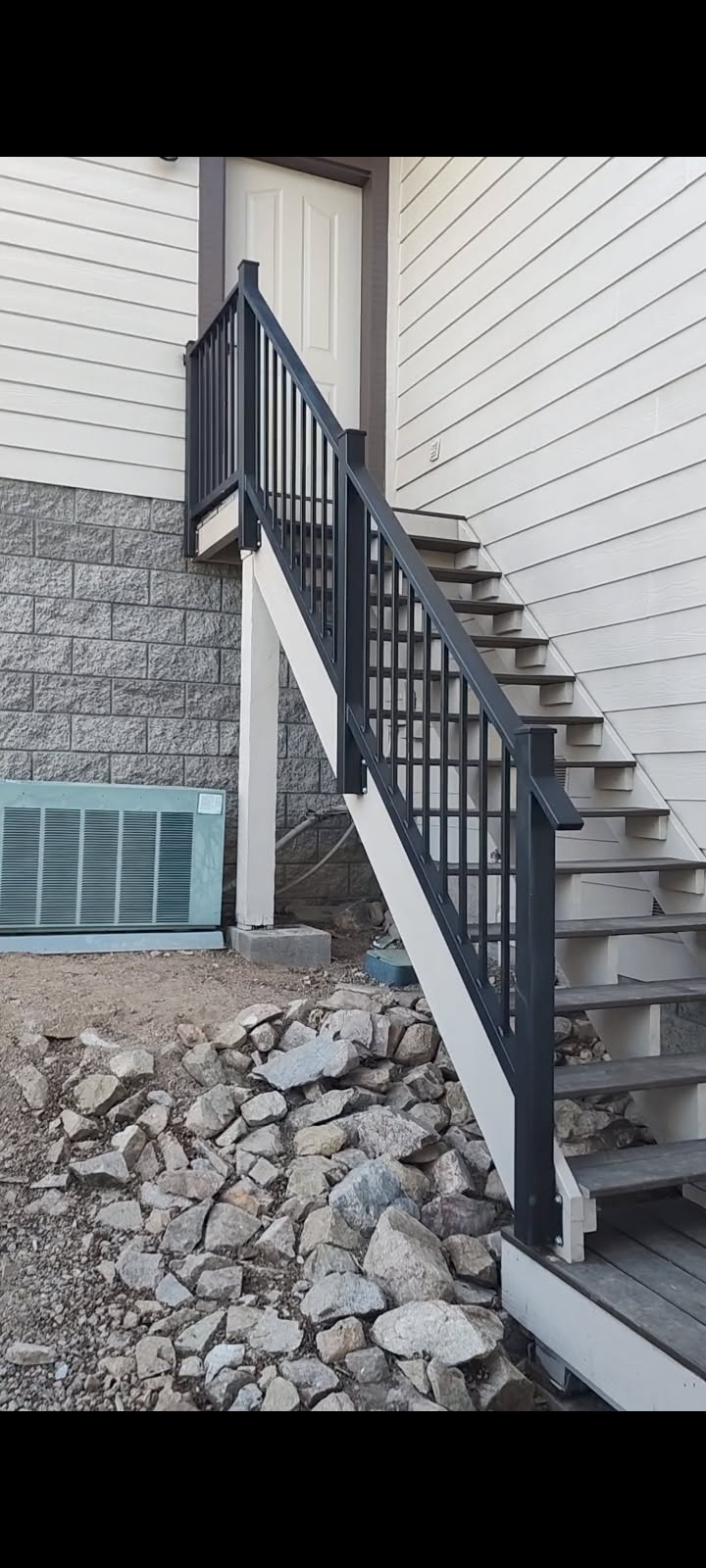 Exterior staircase with black railing and white supports. Rocks surround the base.