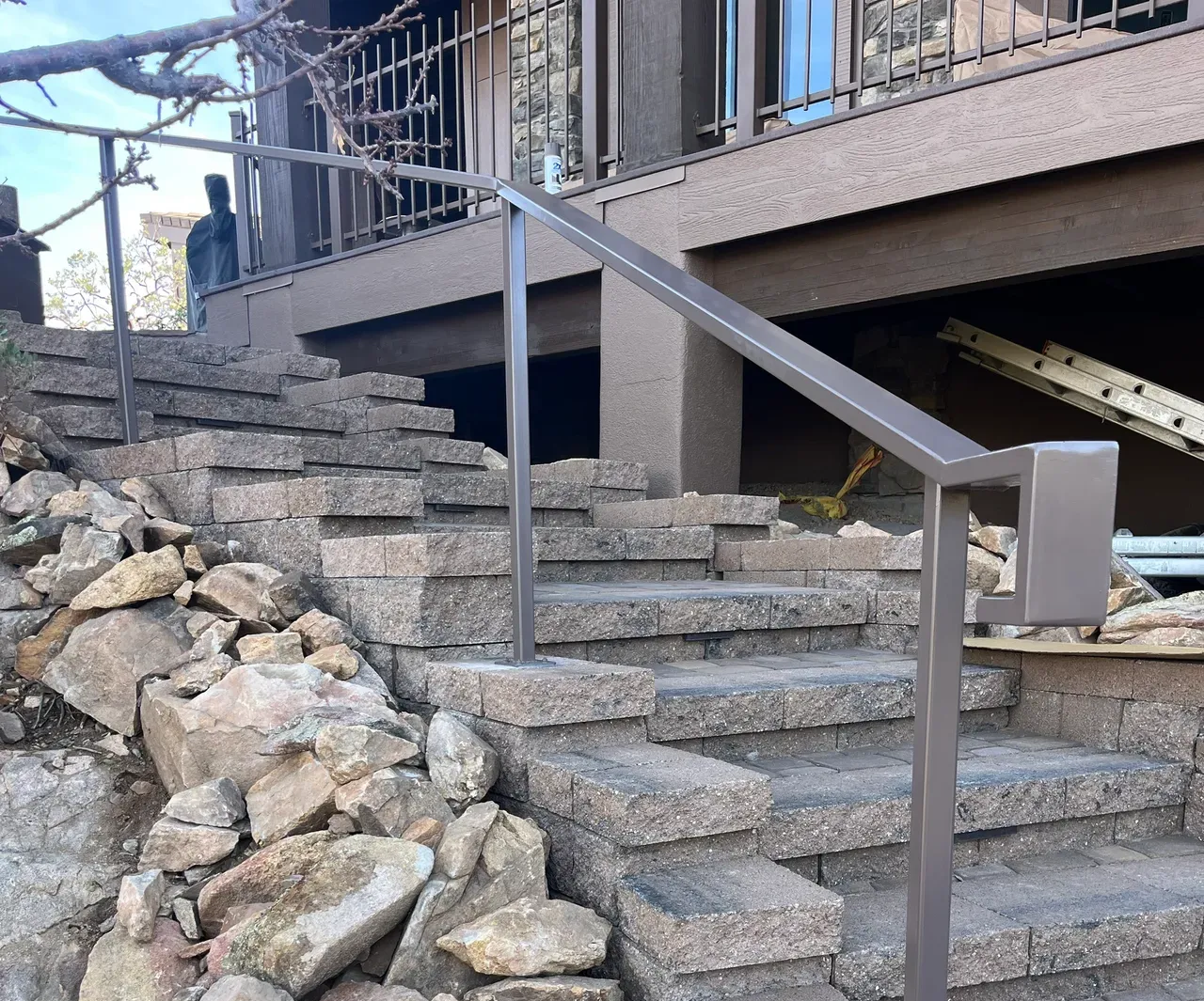 Stone steps with a metal handrail leading to a building's entrance. Surrounding rocks on the left.