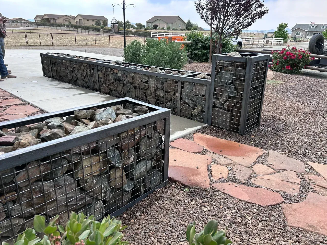 Gabion stone walls with a metal frame in a yard with a stone path.