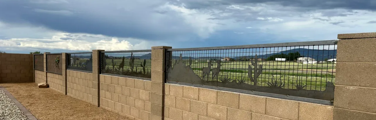 A low, tan brick wall with decorative metalwork atop; green field and stormy sky in the background.