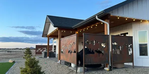 Outdoor patio with metal screens, string lights, gravel, and a white house with a black roof.