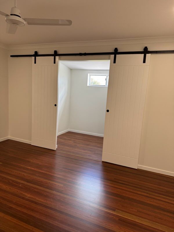A bedroom with sliding barn doors and a ceiling fan — Red Emperor Constructions in Cannonvale, QLD