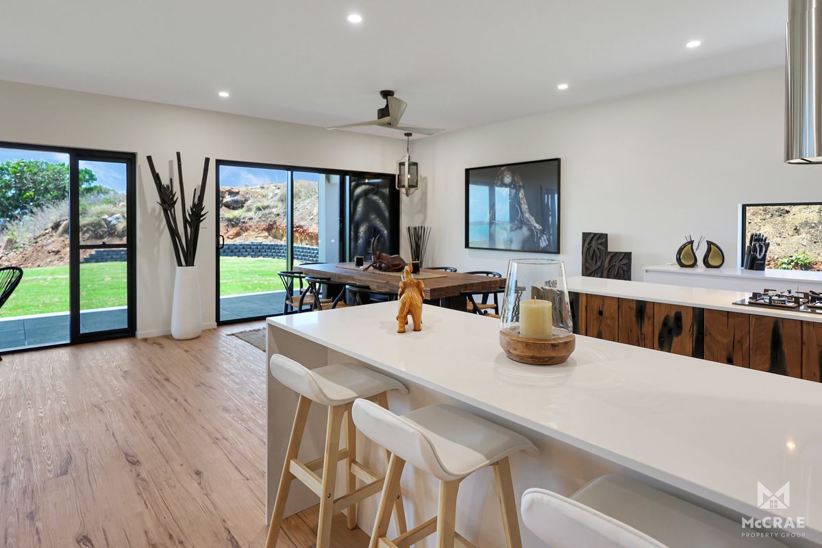 Modern Kitchen With White Island, Wooden Cabinets, Dining Table  — Red Emperor Constructions in Cannonvale, QLD