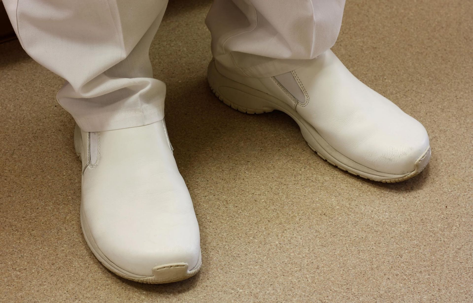 A nurse wearing white shoes and white pants is standing on the floor.
