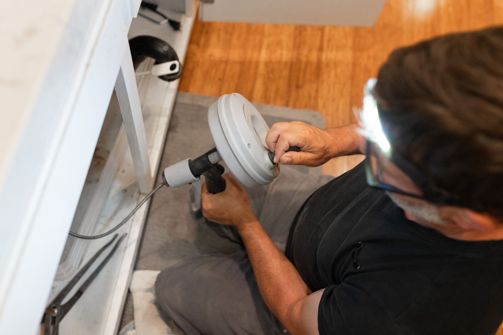 Person tightening a pipe fitting with a wrench in a kitchen cabinet area