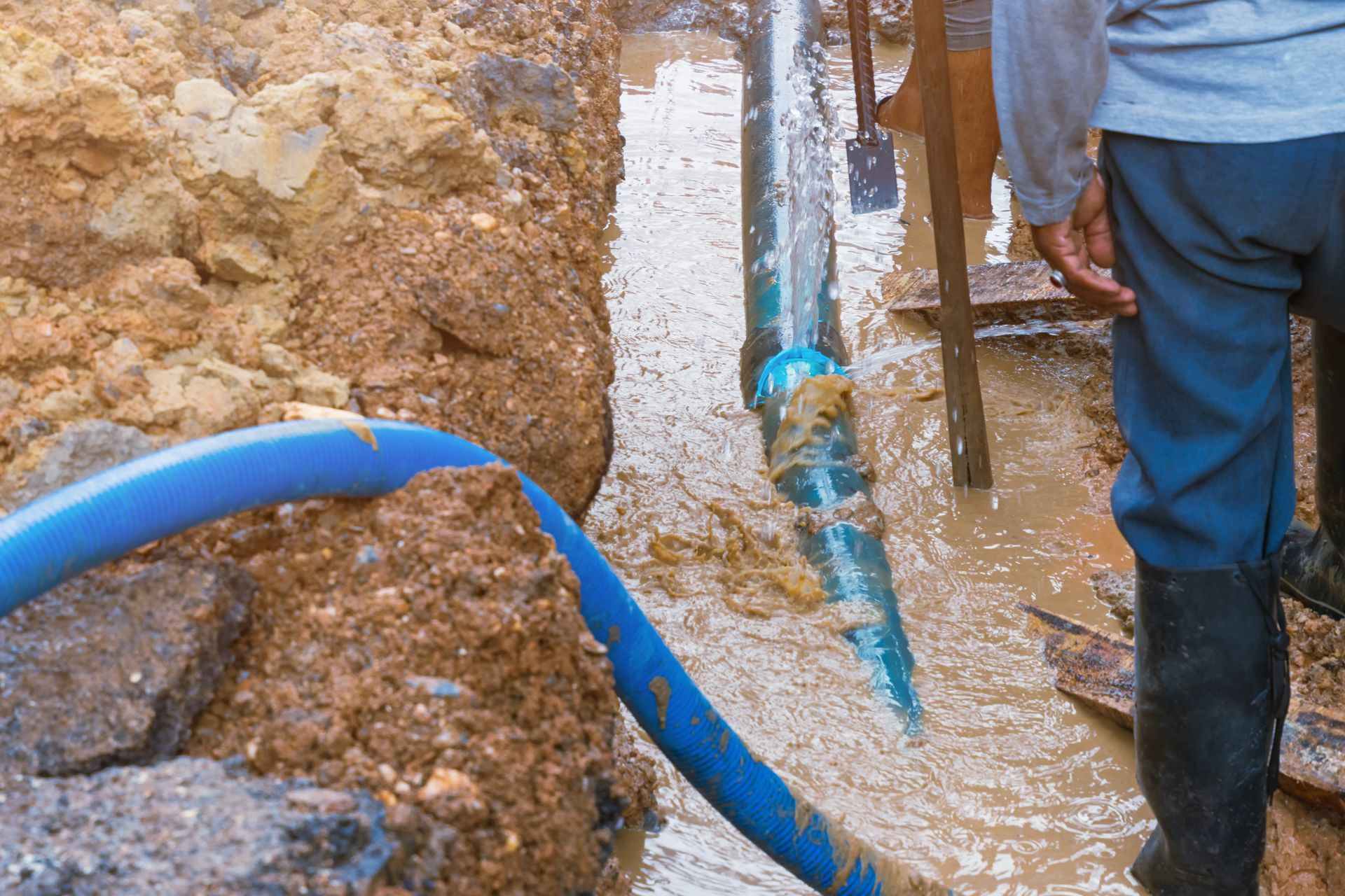 Workers repairing a muddy trench with blue hoses and pipes in an excavation site