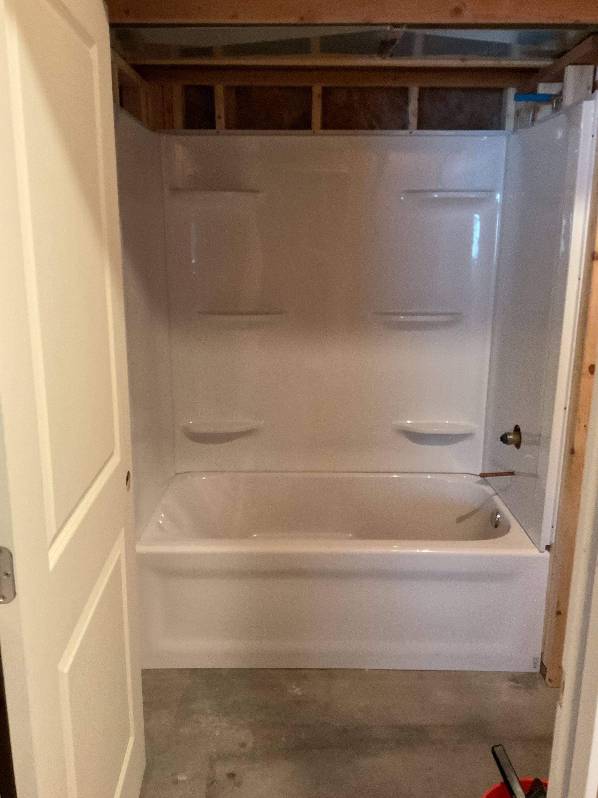 Empty bathroom with a white shower/tub, beige walls, and exposed ceiling framing.