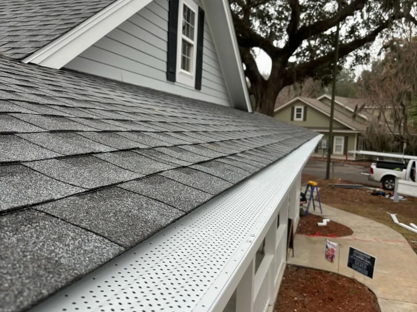 Close-up of a gray shingled roof with white gutters on a suburban house under construction.