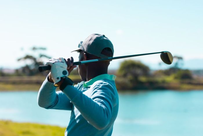 Golfer swinging club on course near water.
