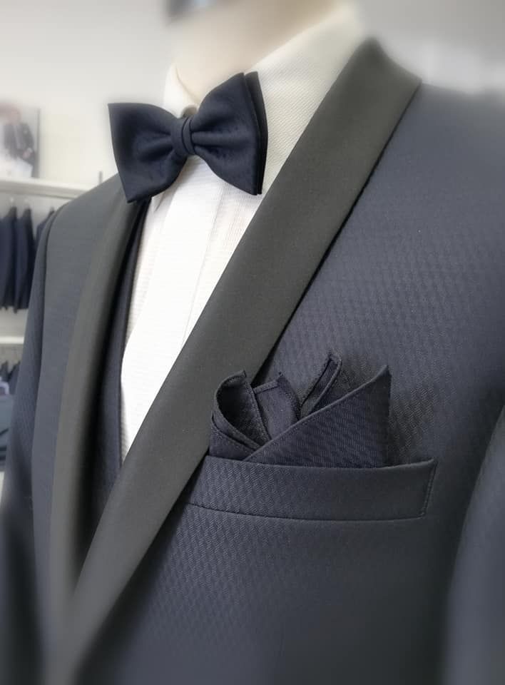 Giacca da smoking scura con papillon e fazzoletto da taschino su un manichino o in vetrina.