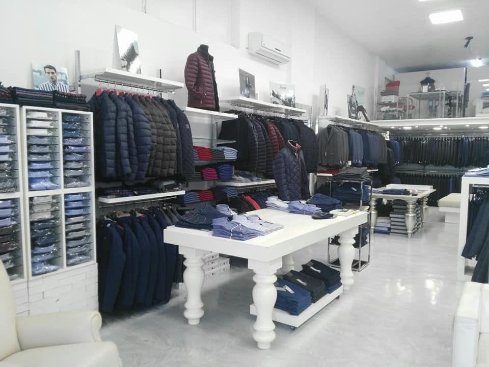 Interno di un negozio di abbigliamento con scaffali pieni di giacche, camicie piegate e tavoli espositivi bianchi.