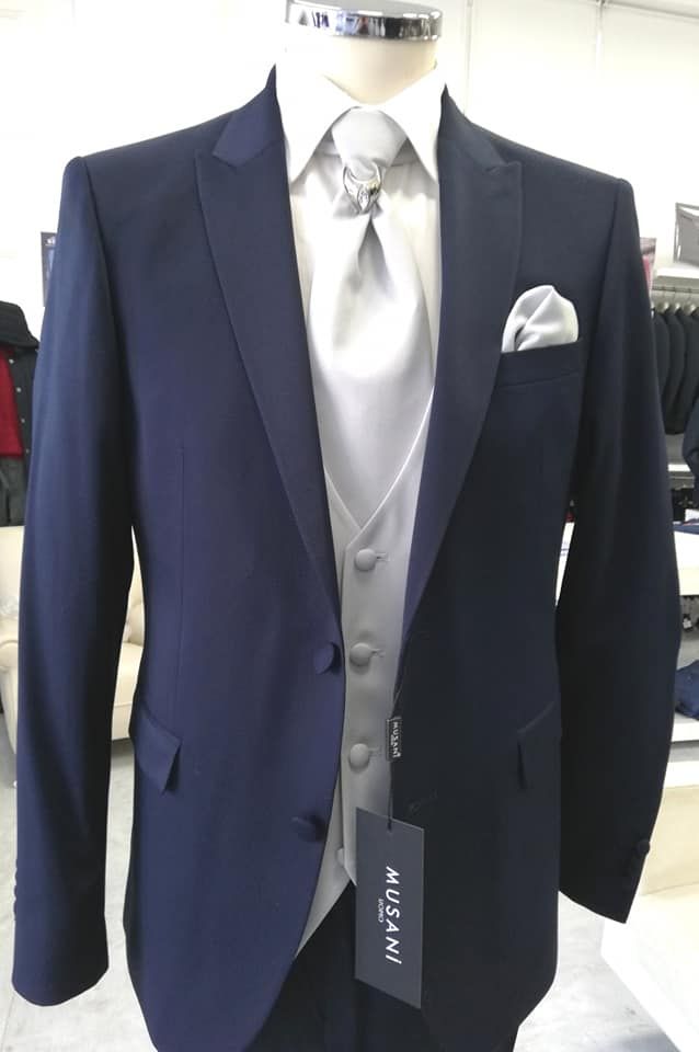 Giacca da completo blu navy con gilet, cravatta e fazzoletto da taschino argentati su un manichino in un negozio