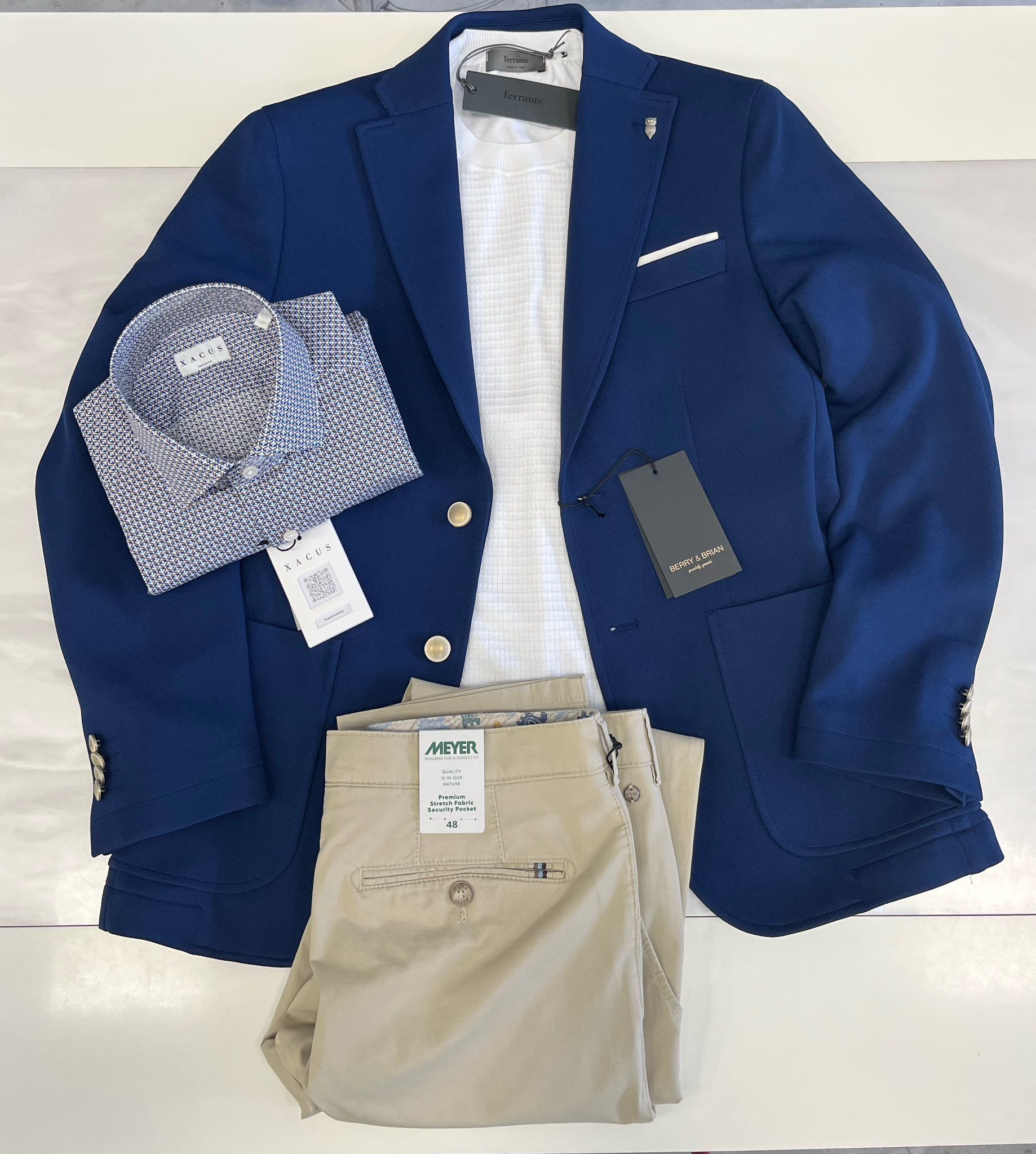 Blazer blu navy con camicia bianca e pantaloni beige disposti su una superficie piana.