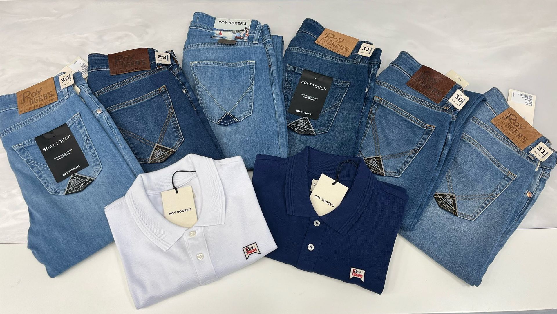 Jeans piegati di vario tipo e due polo, una azzurra e una blu scuro, su sfondo bianco.